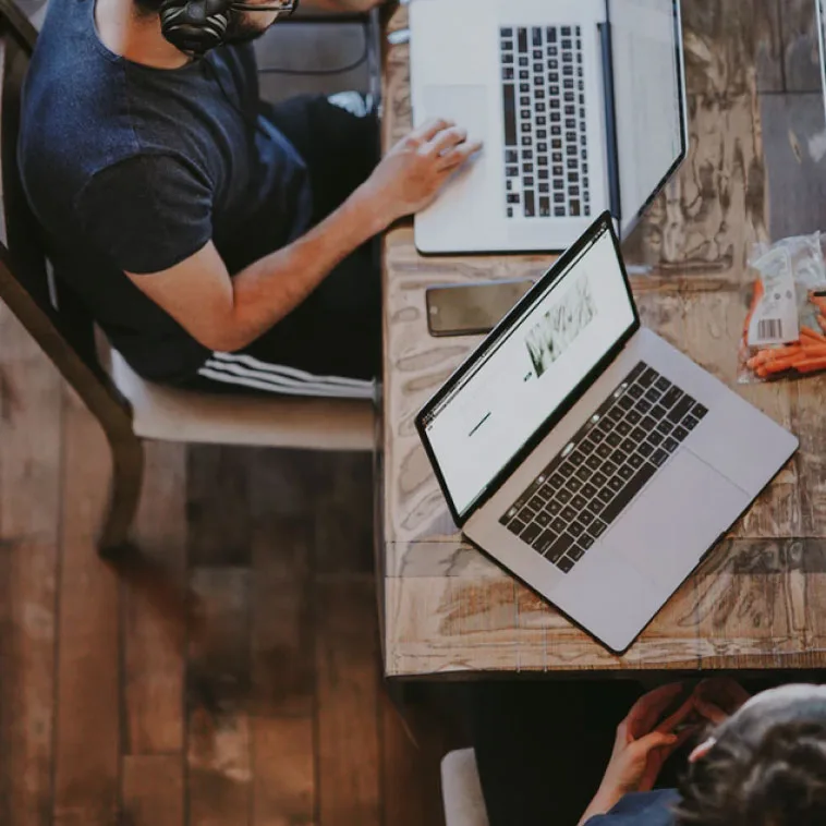 Overhead view of two laptops and notepad on a wooden desk
